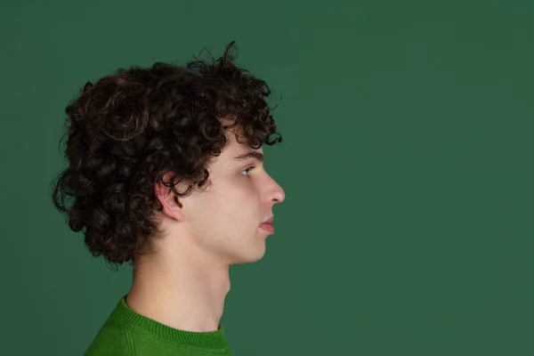 Ausgeschnittene Seitenansicht Porträt eines jungen Mannes in grünem Pullover, der isoliert über dunkelgrünen Hintergrund wegschaut — Stockfoto