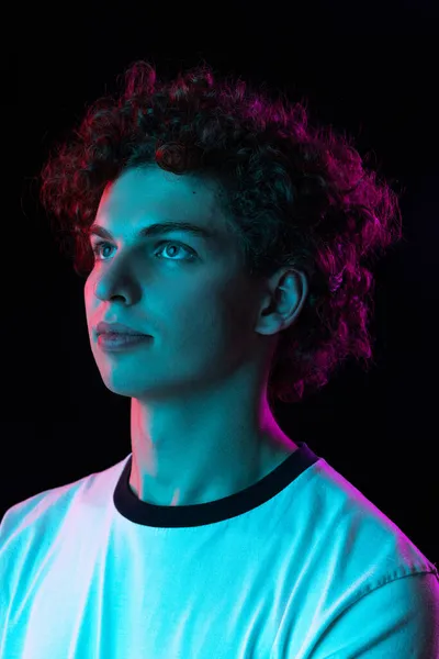 Ausgeschnittenes Porträt eines jungen Mannes in weißem T-Shirt, der isoliert über schwarzem Hintergrund im Neonlicht nach oben blickt — Stockfoto