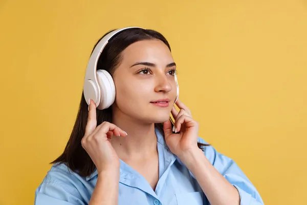 Portrait recadré de jeune belle femme en chemise bleue écoutant de la musique dans des écouteurs isolés sur fond jaune — Photo