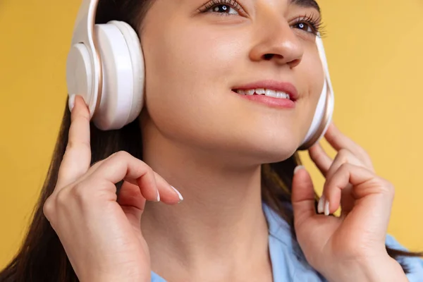 Gros plan portrait de jeune belle femme en chemise bleue écoutant de la musique dans des écouteurs isolés sur fond jaune — Photo