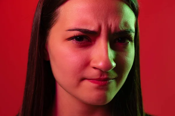 Close-up retrato de jovem bela mulher posando, fazendo rosto rabugento isolado sobre fundo vermelho em luzes de néon — Fotografia de Stock