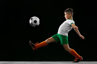 Siyah arka planda izole edilmiş çocuk, çocuk, üniformalı futbolcu portresi. Yan görünüm