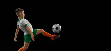 Siyah arka planda izole edilmiş çocuk, çocuk, üniformalı futbolcu portresi. Penaltı atışı. El ilanı