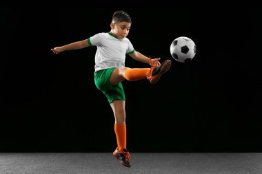 Çocuk, çocuk, üniformalı futbolcu, topun tekmelenmesi, siyah arka planda izole edilmiş..