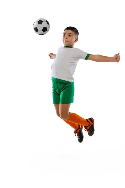 Retrato completo de menino, criança, jogador de futebol em treinamento uniforme, chutando bola com peito em um salto isolado sobre fundo branco. — Fotografia de Stock