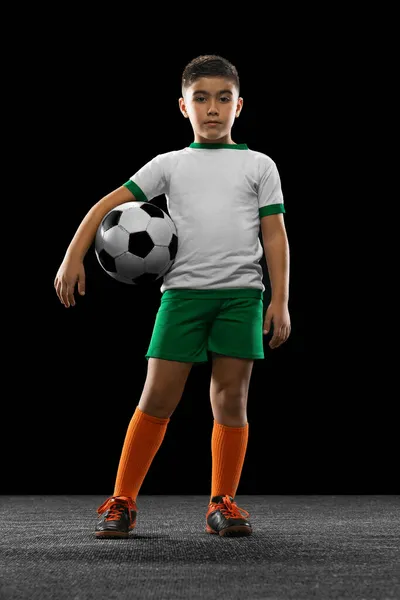 Retrato completo de menino, criança, jogador de futebol em uniforme posando com bola isolada sobre fundo preto. Guarda-redes — Fotografia de Stock