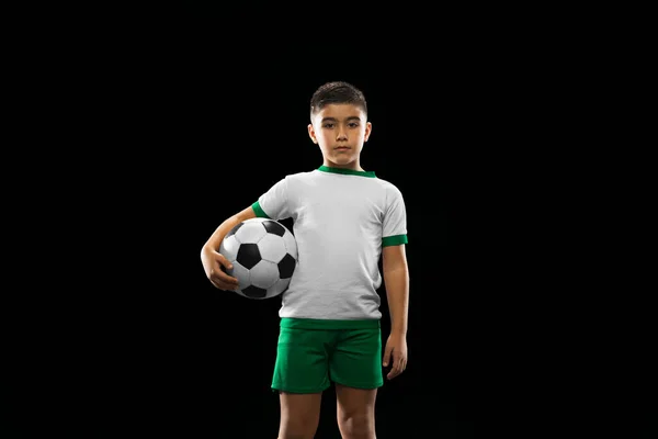 Retrato recortado de niño, niño, jugador de fútbol en uniforme posando con pelota aislada sobre fondo negro. Infancia activa —  Fotos de Stock