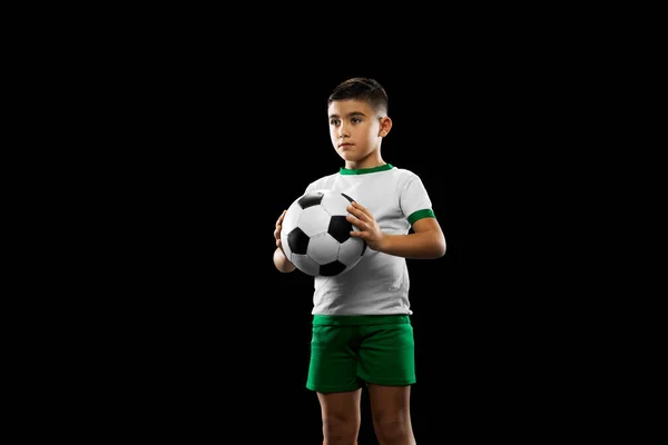 Καλλιεργημένο πορτραίτο αγοριού, παιδιού, ποδοσφαιριστή με στολή ποζάροντας με μπάλα απομονωμένη σε μαύρο φόντο. — Φωτογραφία Αρχείου