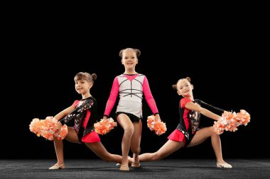 Üç kızın tam boy portresi, siyah arka planda izole edilmiş ponpon pon kostüm eğitimi alan ponpon kızlar.