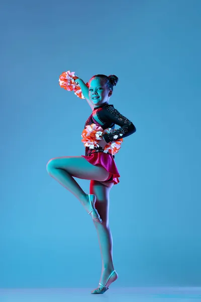 Ganztägiges Porträt der schönen Mädchen, Cheerleader-Training, Durchführung in hellem Body mit Bommel-Pons isoliert über blauem Hintergrund in Neonlicht — Stockfoto