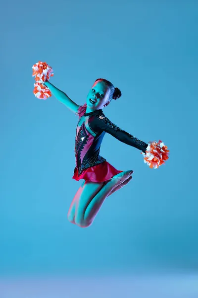 Ganztägiges Porträt der schönen Mädchen, Cheerleader-Training, Durchführung in hellem Body mit Bommel-Pons isoliert über blauem Hintergrund in Neonlicht — Stockfoto