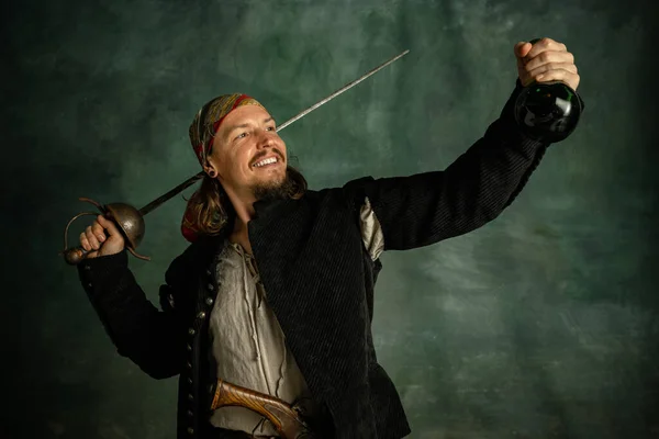 Retrato de un hombre sonriente, pirata medeival sosteniendo botella de ron aislado sobre fondo oscuro. — Foto de Stock