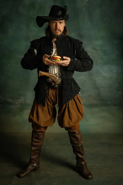 Полный портрет одного жестокого человека, Медейваль пират держа бургер изолированы на темном фоне. — стоковое фото
