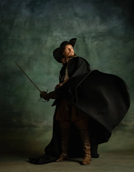 Ganzkörperporträt eines furchtlosen brutalen Mannes, Medaillenpirat mit Hut und Mantel, Schwert isoliert über dunklem Hintergrund. — Stockfoto