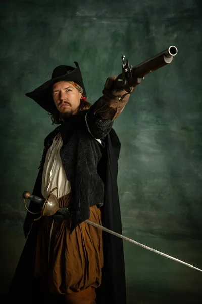 Обрізаний портрет жорстокого переляканого чоловіка, воїна-пірата в вінтажному костюмі з мечем і пістолетом ізольовано на темному тлі . — стокове фото