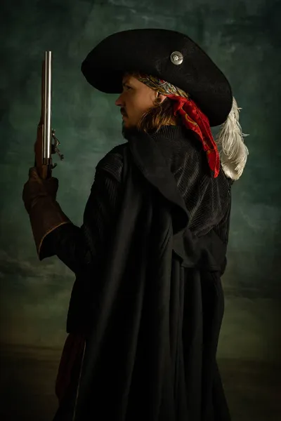 Retrato recortado de hombre aterrador brutal, pirata medeival en traje vintage con espada y pistola aislada sobre fondo oscuro. Vista lateral — Foto de Stock