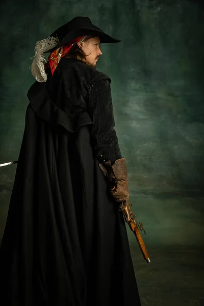 Porträt eines brutalen furchterregenden Mannes, Medaillenpirat im Vintage-Kostüm mit Schwert und Gewehr isoliert vor dunklem Hintergrund. Rückseite — Stockfoto