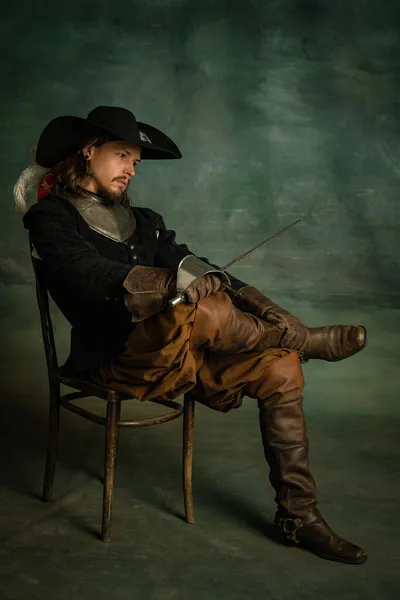 Portrait d'homme brutal horrible, pirate medeival en costume vintage assis et tenant l'épée isolée sur fond sombre. — Photo