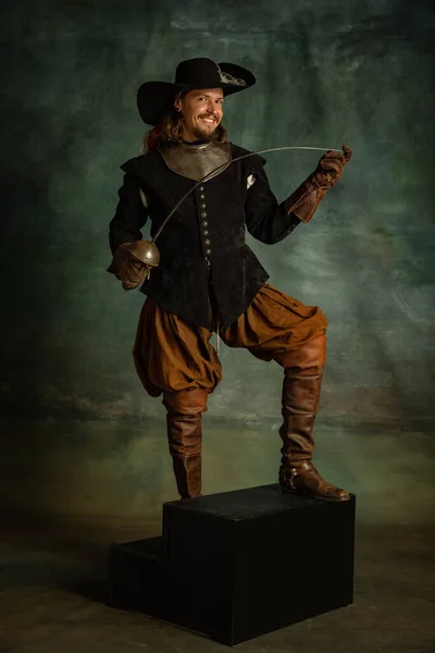 Портрет жестокого ужасающего человека, медейвального пирата в винтажном костюме, держащего меч изолированным на тёмном фоне. — стоковое фото
