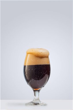 Gri arka planda izole edilmiş koyu köpüklü bira bardağı. Alkol ve parti kavramı