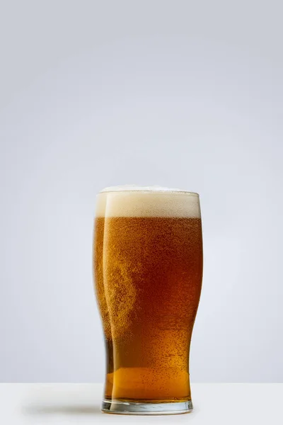 Egy pohár világos habos sör szürke háttérrel. Az alkoholtartalmú italok fogalma — Stock Fotó