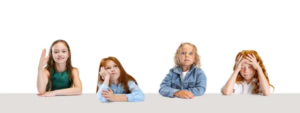 Collage of four children, girls, pupils sitting at the table with different emotions isolated over white background — Stock Photo, Image