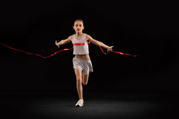 Teljes hosszúságú portré tinédzser lányról, amint átkel a piros szalagon, fekete háttérrel elszigetelve. Nyertes maraton — Stock Fotó