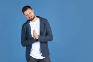 Düşünceli bir adamın portresi mavi arka planda izole edilmiş ellerini ovuşturuyor.