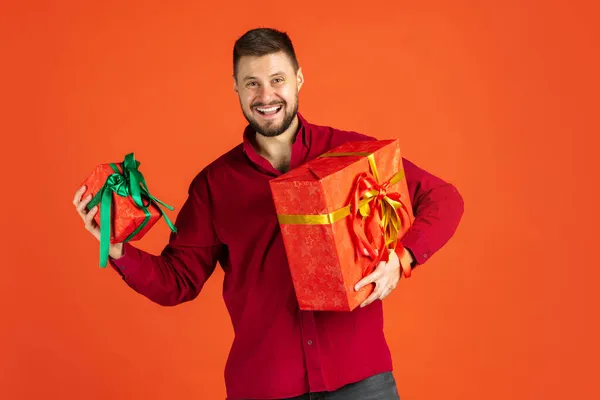 Egy boldog, izgatott férfi portréja, két ajándékdobozzal, piros háttérrel elszigetelve. Közelgő ünnepek — Stock Fotó