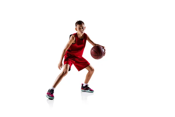 Ganzkörperporträt eines Jungen, Basketballspielers in roter Uniform, der isoliert vor weißem Hintergrund trainiert. Dribbeln — Stockfoto