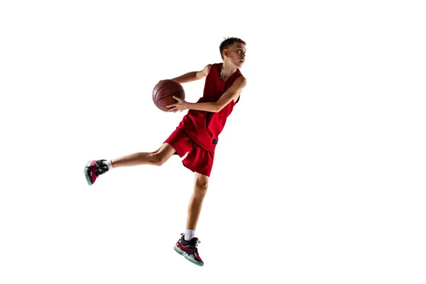 Full-length portrait of teenager, boy in red uniform playeing, training basketball isolated over white background — Stock Photo, Image