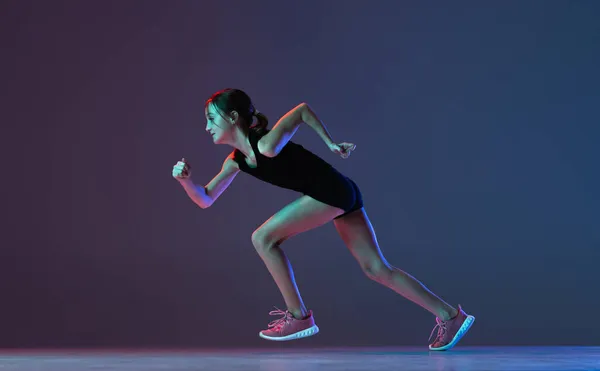 Portrait of girl, professional athlete, runner training isolated over gradient blue purple background in neon — Stock Photo, Image