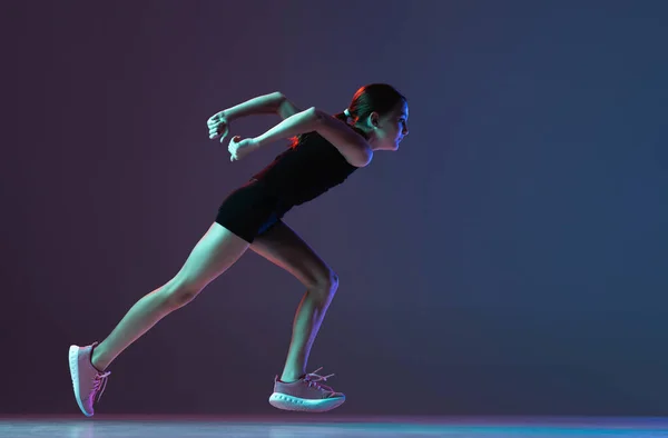 Full-length portrait of concentrated female athlete, girl running, training isolated over gradient blue purple background in neon — Stock Photo, Image