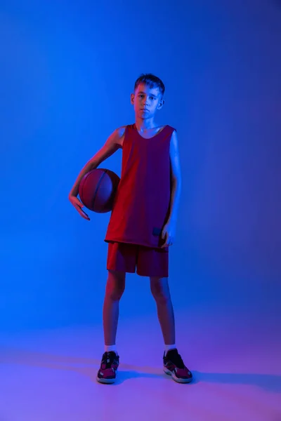 Porträt eines Basketballspielers in Uniform, der isoliert über einem Gefälle posiert, blaulila Hintergrund im Neonlicht — Stockfoto