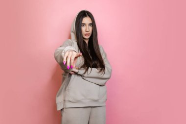 Kamerayı işaret eden, pembe arka planda soyutlanmış genç bir kızın kırpılmış portresi.