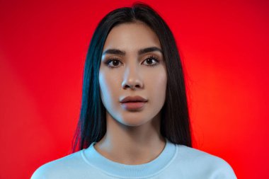 Genç ve güzel bir kızın kesilmiş portresi kameraya bakıyor, sakince kırmızı arka planda izole edilmiş poz veriyor.