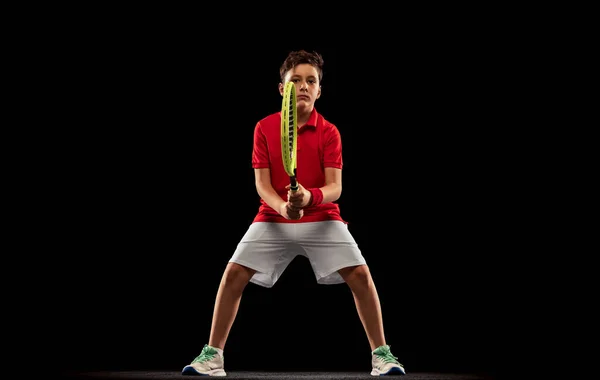 Portrait of boy, tennis player in uniform with racket training isolated over black background — Stock Photo, Image