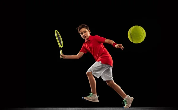 少年の完全な長さの肖像画,運動中のテニス選手,黒の背景に隔離ラケットでボールを蹴ります.得点目標 — ストック写真
