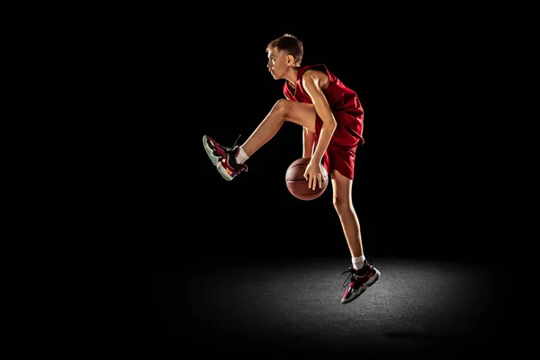 Genç bir çocuğun tam boy portresi, hareket halindeki basketbol oyuncusu, antrenman, dizlerinin altında top sürmek siyah arka planda izole edilmiş. — Stok fotoğraf