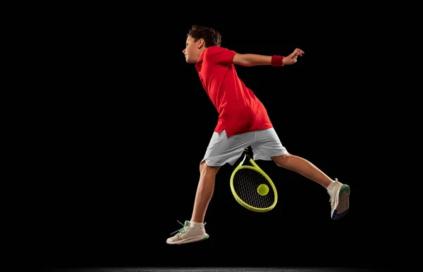 Retrato de menino esportivo, tenista em unifrom, treinando isolado sobre backgound preto. Em movimento — Fotografia de Stock