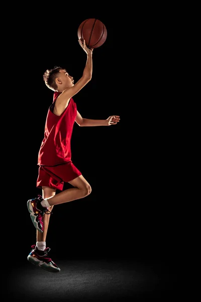 Segnare gol nel salto. Sportivo teen boy, giocatore di basket che lancia palla nel cestino isolato su sfondo nero — Foto Stock