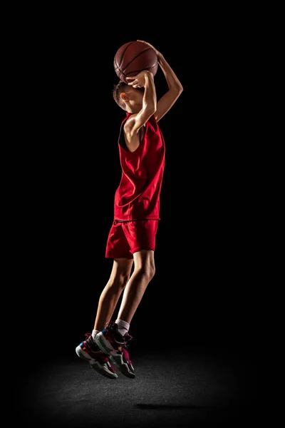 Teljes hosszúságú portré tini fiú, kosárlabda játékos edzés, dobott labdát a kosárba egy ugrás elszigetelt fekete háttér — Stock Fotó