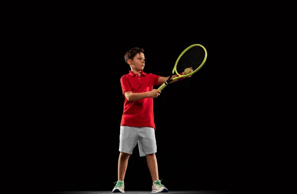 Retrato completo de menino, jogador de tênis em movimento, treinamento, servindo bola isolada sobre fundo preto — Fotografia de Stock