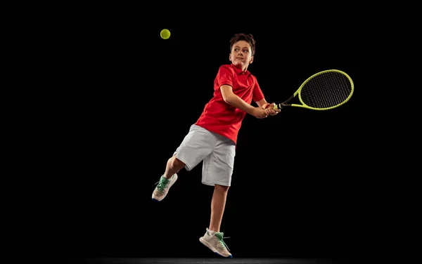 Pełnowymiarowy portret chłopca, tenisista w ruchu, piłka z rakietą odizolowana od czarnego backgound 'a — Zdjęcie stockowe
