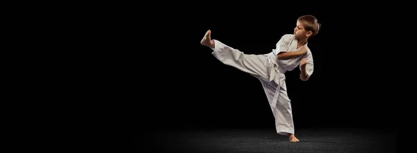 Retrato completo de rapazinho praticando arte marcial isolado sobre fundo preto. Pontapé lateral. Folheto — Fotografia de Stock