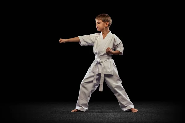 Полнометражный портрет маленького мальчика, спортсмена, стоящего в передней стойке, высокого удара позы изолированы на черном фоне — стоковое фото