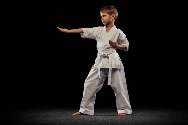 Portrait of little boy, sportsman training martial art isolated over black background — Stock Photo, Image