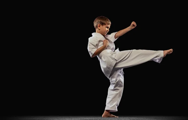 Retrato completo de menino, desportista praticando arte marcial isolado sobre fundo preto. Pontapé lateral — Fotografia de Stock