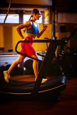 Koşu bandında kardiyo yapan genç bir kadının tam boy portresi. Beden eğitimi. Yan görünüm