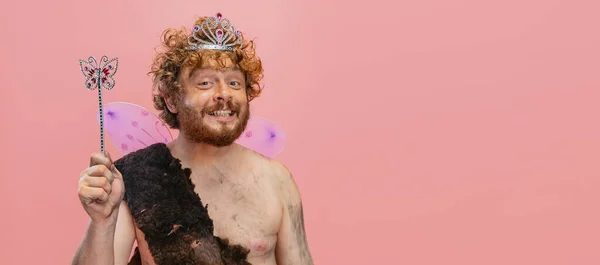 ピンクの背景の上に隔離された小さな妖精の冠を身に着けているネアンデルタールの文字で陽気な幸せな男のトリミングされた肖像画 — ストック写真